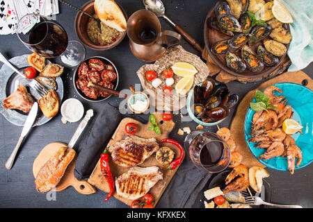 Overhead of dinner table. Assorted delicious grilled barbecue meat and seafood with vegetable. Pork grilled steaks, grilled salmon trout, mussels, shr Stock Photo