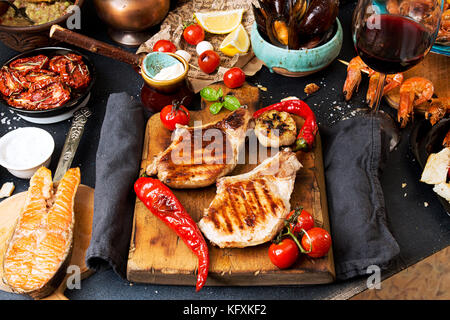 Overhead of dinner table. Assorted delicious grilled barbecue meat and seafood with vegetable. Pork grilled steaks, grilled salmon trout, mussels, shr Stock Photo