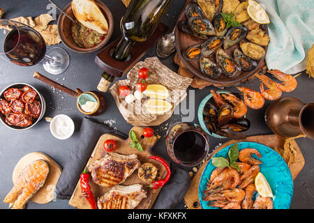 Overhead of dinner table. Assorted delicious grilled barbecue meat and seafood with vegetable. Pork grilled steaks, grilled salmon trout, mussels, shr Stock Photo