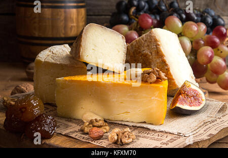 Food composition with blocks of moldy cheese, dried dates, grape bunch, olives, figs on old wooden background. Stock Photo