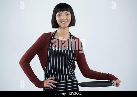 Portrait of smiling waitress holding empty tray against white background Stock Photo