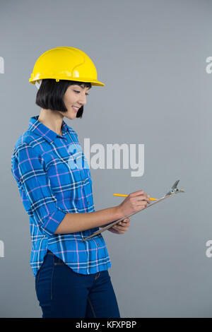 Smiling female architect writing on clipboard against grey background Stock Photo