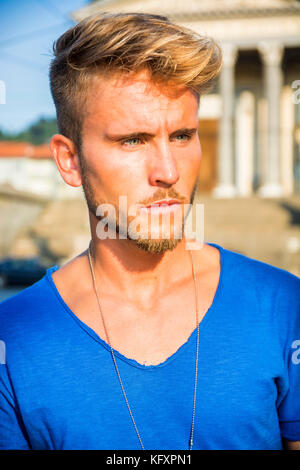 Handsome blond, blue eyed young man leaning against stone wall outdoor and looking to a side in Turin, Italy Stock Photo