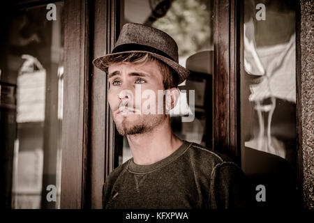Portrait of blond haired handsome young man with fedora hat. An old train station is behind him in Italian town Stock Photo