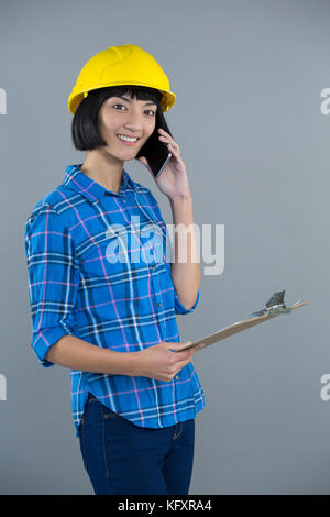 Smiling female architect talking on mobile phone against grey background Stock Photo