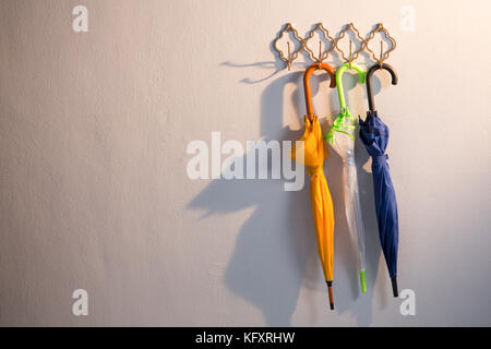Colorful umbrellas hanging on hook against white wall Stock Photo