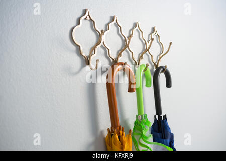 Colorful umbrellas hanging on hook against white wall Stock Photo