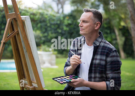 Smiling man painting on canvas in garden Stock Photo