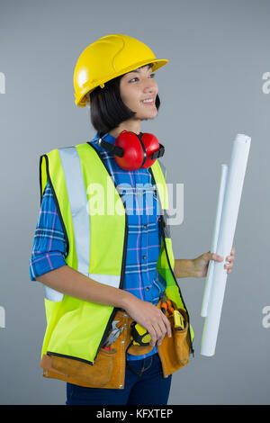 Thoughtful female architect holding blueprint against grey background Stock Photo