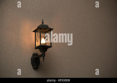 A yellow glass lantern hanging on a gray old wall. Bright glowing lantern illuminating the wall of an ancient building Stock Photo