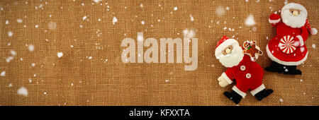 Snow falling against stuffed santa claus on burlap Stock Photo