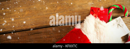 Snow falling against wrapped gift box and candy cane in stocking on wooden table Stock Photo