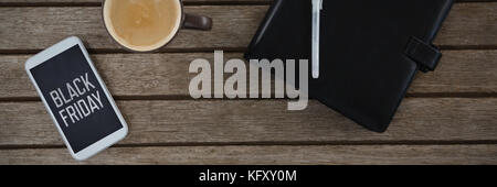 Mobile phone, coffee, pen and organizer on wooden plank against black friday advert Stock Photo