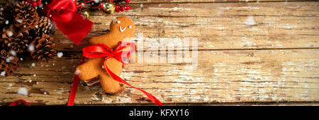 Snow falling against gingerbread cookie tied with ribbon on wooden plank Stock Photo