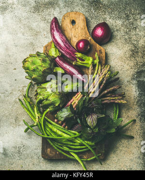 Flat-lay of green and purple vegetables on board, grey background Stock Photo