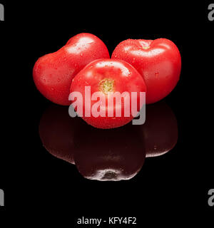 Three whole large red tomatoes isolated on black glossy background with real reflection. Side view Stock Photo