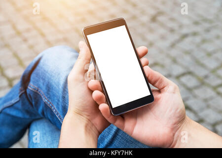 Man uses his Mobile Phone outdoor, close up. Image of young man with mobile smart phone sitting on the bench. Stock Photo