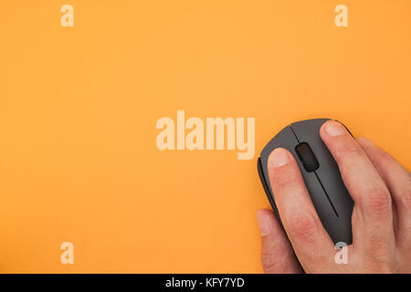Person using wireless computer mouse on yellow background. Close up. Stock Photo