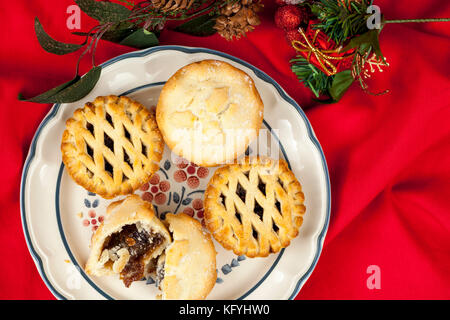 Plated lattice top mince pies at christmas on a ruffled red table cloth with some festive seasonal decorations Stock Photo