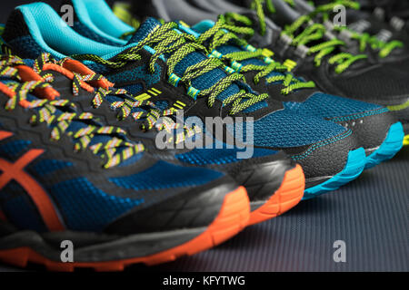 Three pairs of colourful exercise trainers / running shoes lined up in a row on a gym floor Stock Photo