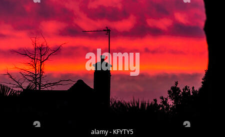 A shot of a silhouetted house against an orange sunset. Stock Photo