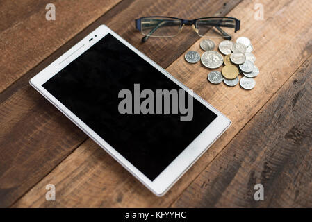 Digital tablet on wooden table backgorund with coins and spectacles. lifestyle and technology concept. Stock Photo
