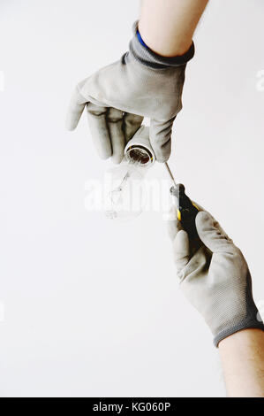 Two male hands holding light bulb and a screwdriver Stock Photo