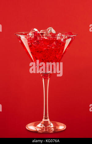 glass with red cocktail and ice cubes on red background. Stock Photo
