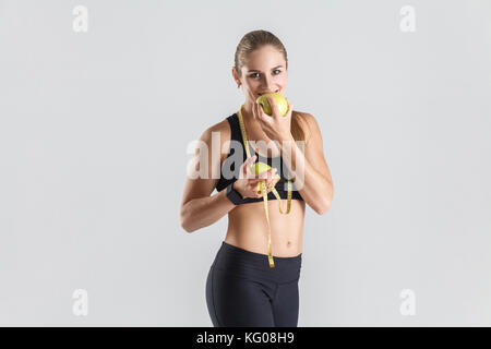 Woman eating green apple, toothy smiling and looking at camera. Studio shot, gray background Stock Photo
