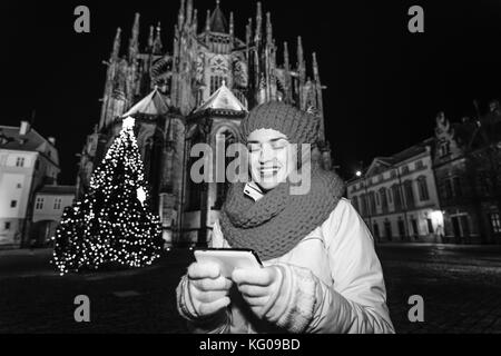 Magic on streets of the old town at Christmas. happy young tourist woman in red hat and scarf near Christmas tree against St. Vitus Cathedral in Pragu Stock Photo