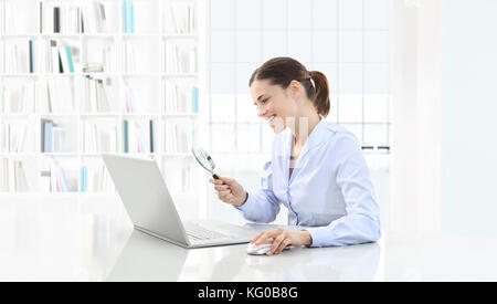 smiling woman in office search on computer with magnifying glass sitting at the desk Stock Photo