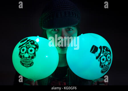 Pretty Mexican woman in knit cap holding lighted balloons with skulls during day of the dead or day of the dead festival Stock Photo