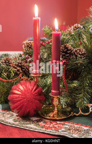 Christmas display with brass candlesticks, greenery, pine cones, and a red ball ornament Stock Photo