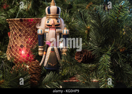 Christmas background display with a nutcracker and red candle holder surrounded by greenery and pine cones Stock Photo