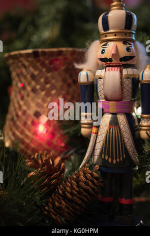 Christmas display with a nutcracker and pine cones in the foreground and a red candle holder in soft focus behind Stock Photo