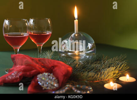 Two glasses of wine, candle, beads, brooch and a branch of a Christmas tree on a green background Stock Photo