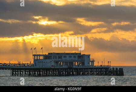 Sun rising with the suns rays shining through clouds on a cloudy morning at Worthing Pier in Worthing, West Sussex, England, UK. Stock Photo