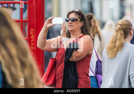 White female tourist taking photos using a smartphone camera in a crowded area in the UK. Stock Photo