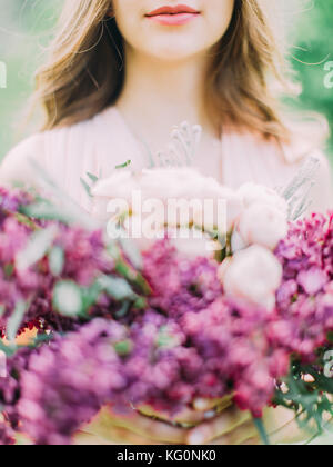 The part of the woman face behind the blurred bouquet consisted of pink roses and purple flowers. Stock Photo