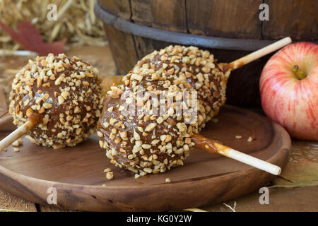 Caramel apples coated with nuts on a wooden plate Stock Photo