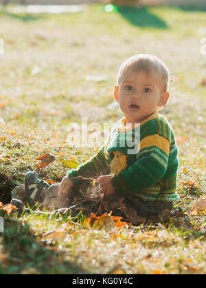 A little 1 year old baby boy sitting on autumn ground park on sunset. Child smiling and laughting, Adorable child. Stock Photo