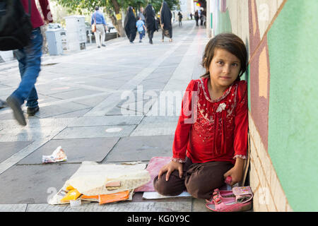 Tehran, IRAN - August 16, 2017 A lonely  little girl selling small tissue packages at street pavement in front of painted wall Stock Photo