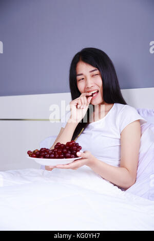 woman with red grape on bed in the bedroom Stock Photo