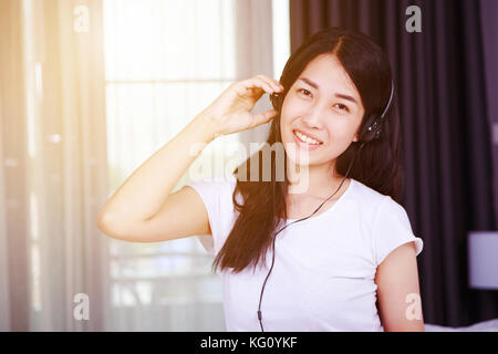 woman in headphones listening to music from smartphone with the window background Stock Photo