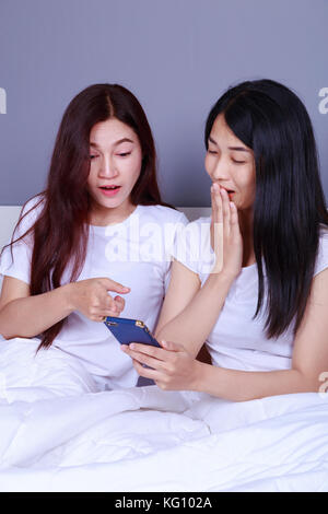 two shocked woman using a phone in her hand on bed in the bedroom Stock Photo