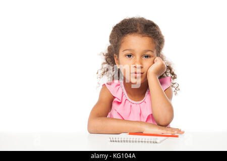 Education. Close up portrait of african little girl is sitting at the table with a notebook for drawing, isolated on white background Stock Photo