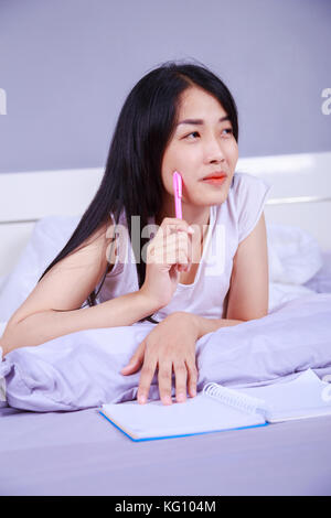 woman thinking and writing a book on her bed in the bedroom Stock Photo