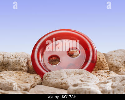 Bright red button among the stones with blue gradient background. Stock Photo