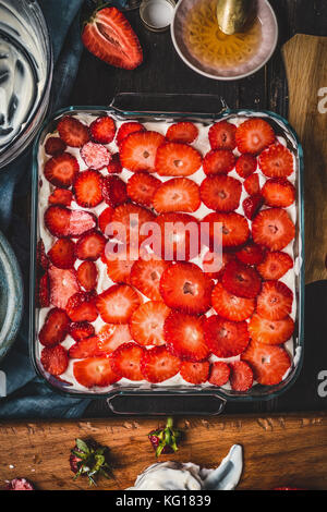 Strawberries cake preparation in glass dish on rustic kitchen table background, top view Stock Photo