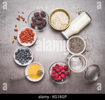 Various Healthy breakfast ingredients with superfood: chia seeds, goji berries, oatmeal , fresh berries , honey and milk or yogurt on grey background, Stock Photo